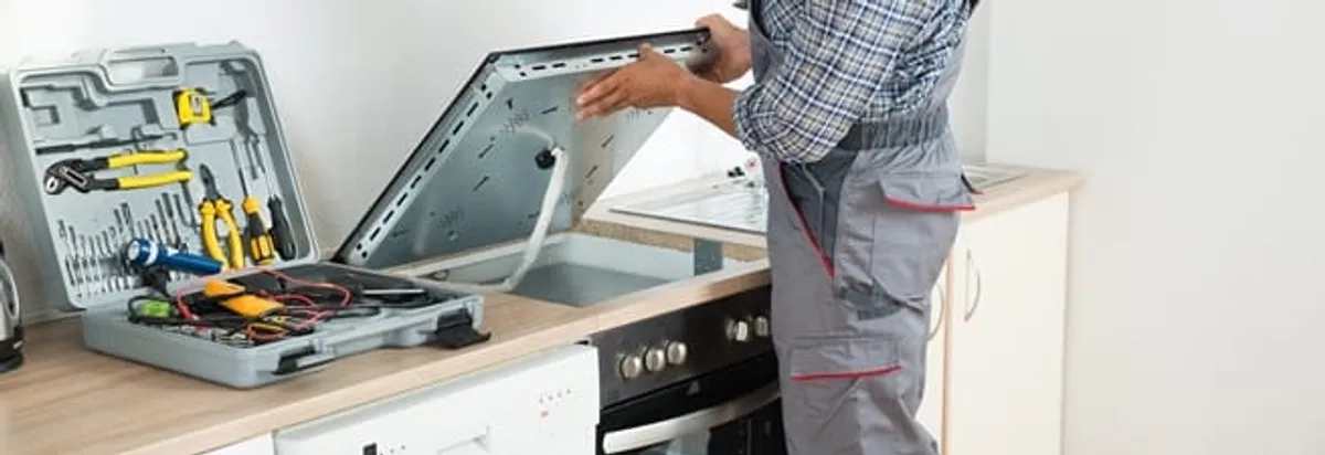 Cooktop repair technician lifting a built-in stovetop for service in Seattle, WA