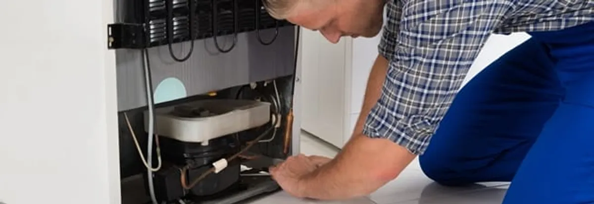 Refrigerator repair technician servicing the compressor and condenser area in Seattle, WA